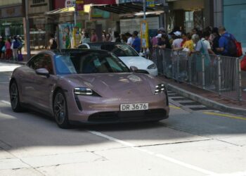 A rose gold porsche drives down a city street.