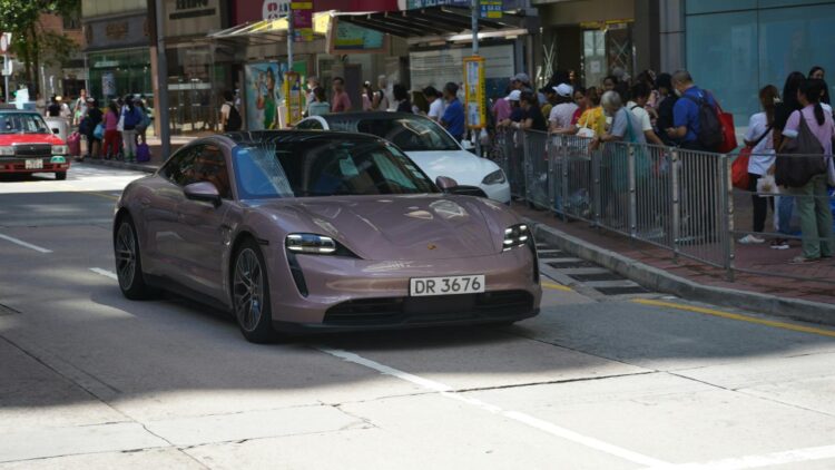 A rose gold porsche drives down a city street.