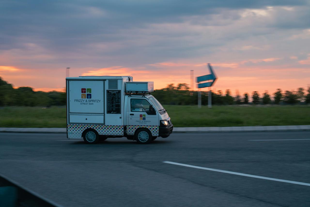 a white truck driving down a street next to a lush green field