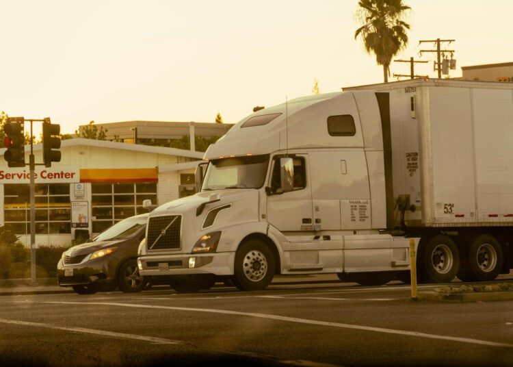 A semi-truck crosses a road next to a car.